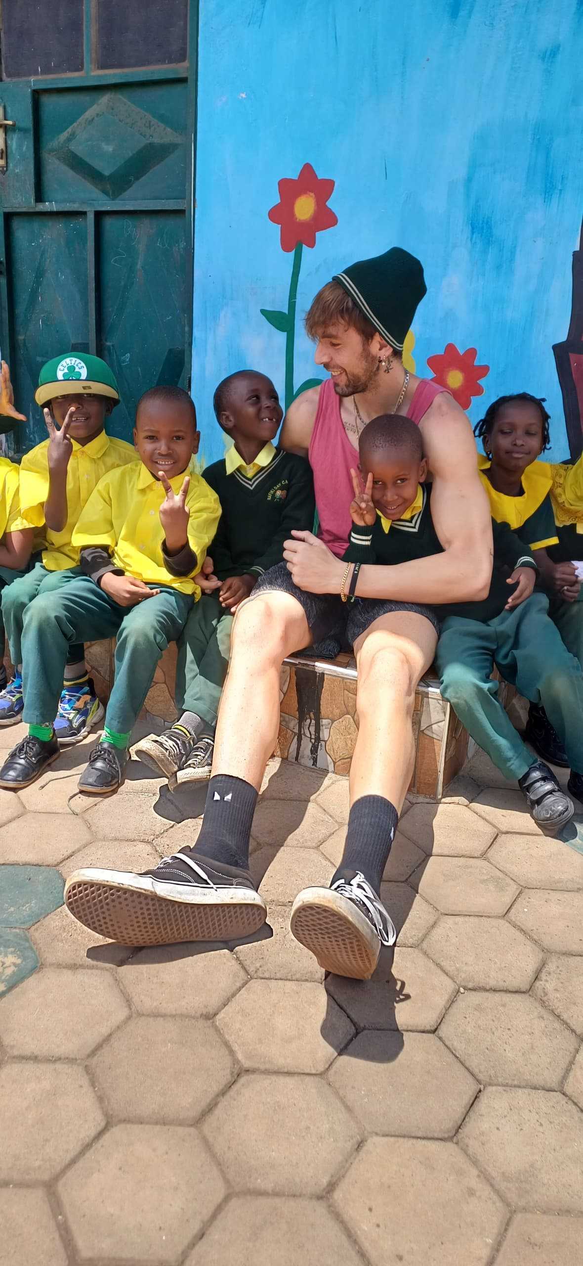 Davide Momi sitting with children outside a colorful school building.